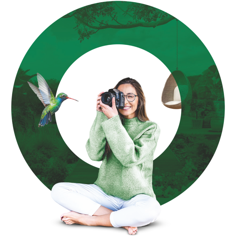 Novax Genius Classic Progresif gözlük camı kullanıcı ürün görseli; kamerayla dış mekanda aktif kadın. Novax Genius Classic Progressive eyeglass lens lifestyle image.
